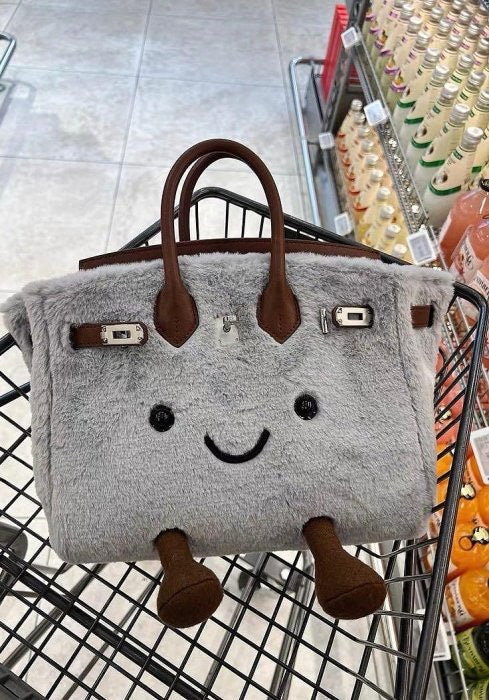 Gray plush smiley face handbag with brown handles and cute 3D legs in shopping cart