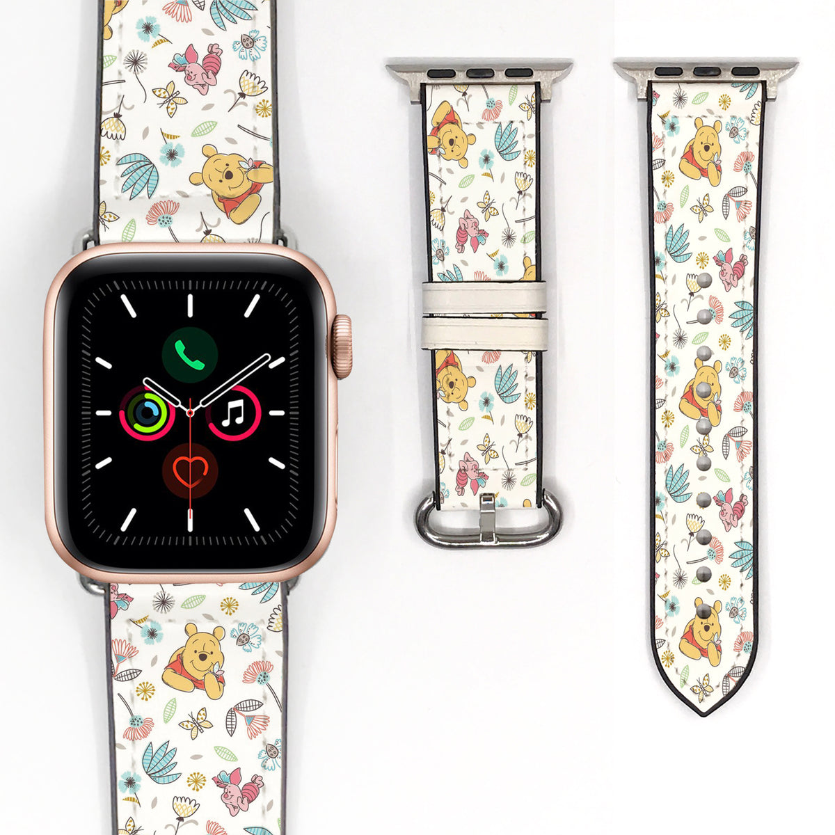 Close-up of a cream character-print Apple Watch band with colorful flowers, leaves, and silver-tone hardware.