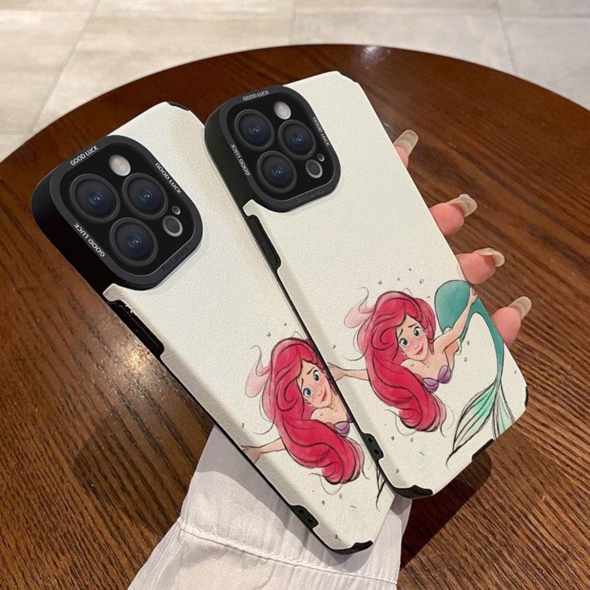 Phone case with mermaid design held by a hand on a wooden surface