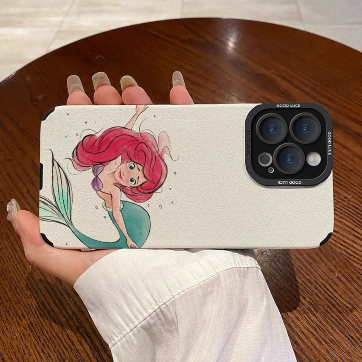 Phone case with a cartoon mermaid design held by a person on a wooden surface