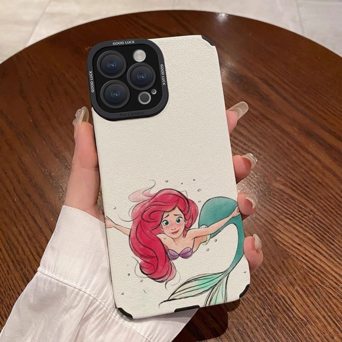 Phone case with a mermaid design held by a hand on a wooden surface