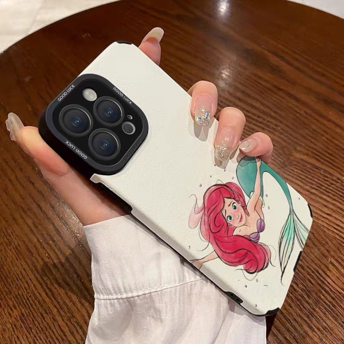 Phone case with a mermaid design held by a hand on a wooden surface