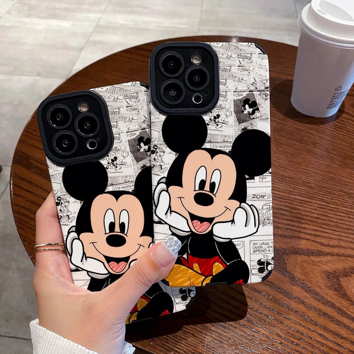 iPhone case with Mickey Mouse design held by a person on a wooden table.