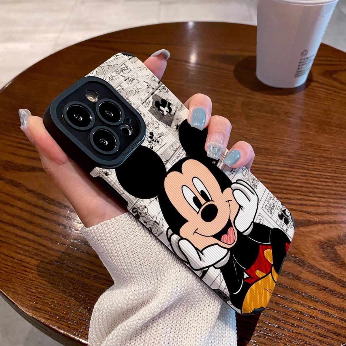 iPhone case with Mickey Mouse design held by a person on a wooden table.