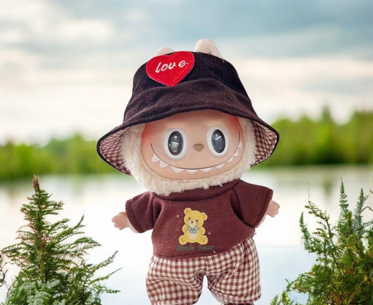 Stuffed toy with a hat and outfit standing outdoors near water and trees