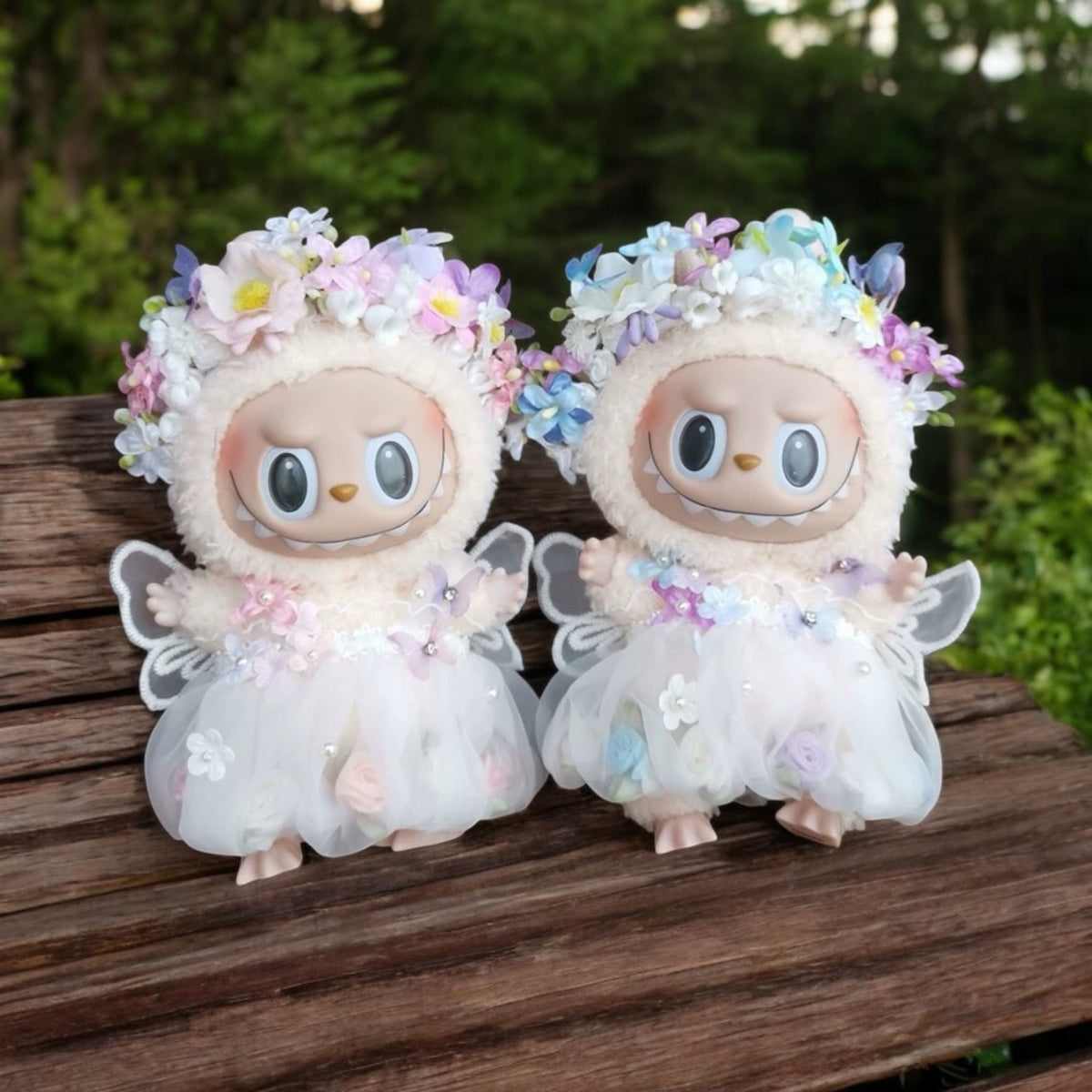 Two plush toys with floral crowns sitting on a wooden surface outdoors.