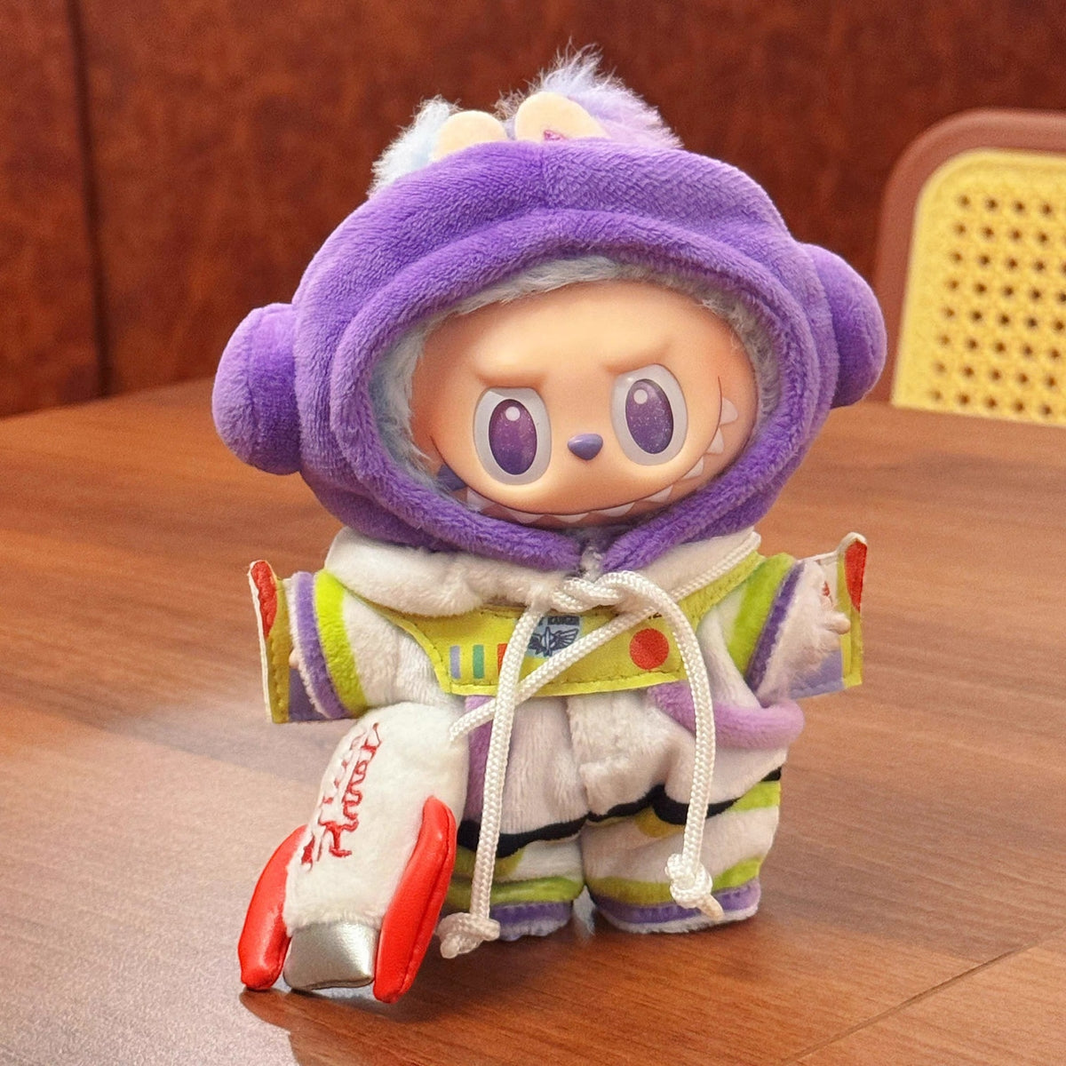 Plush toy buzz lightyear with a purple hood and colorful outfit on a wooden surface