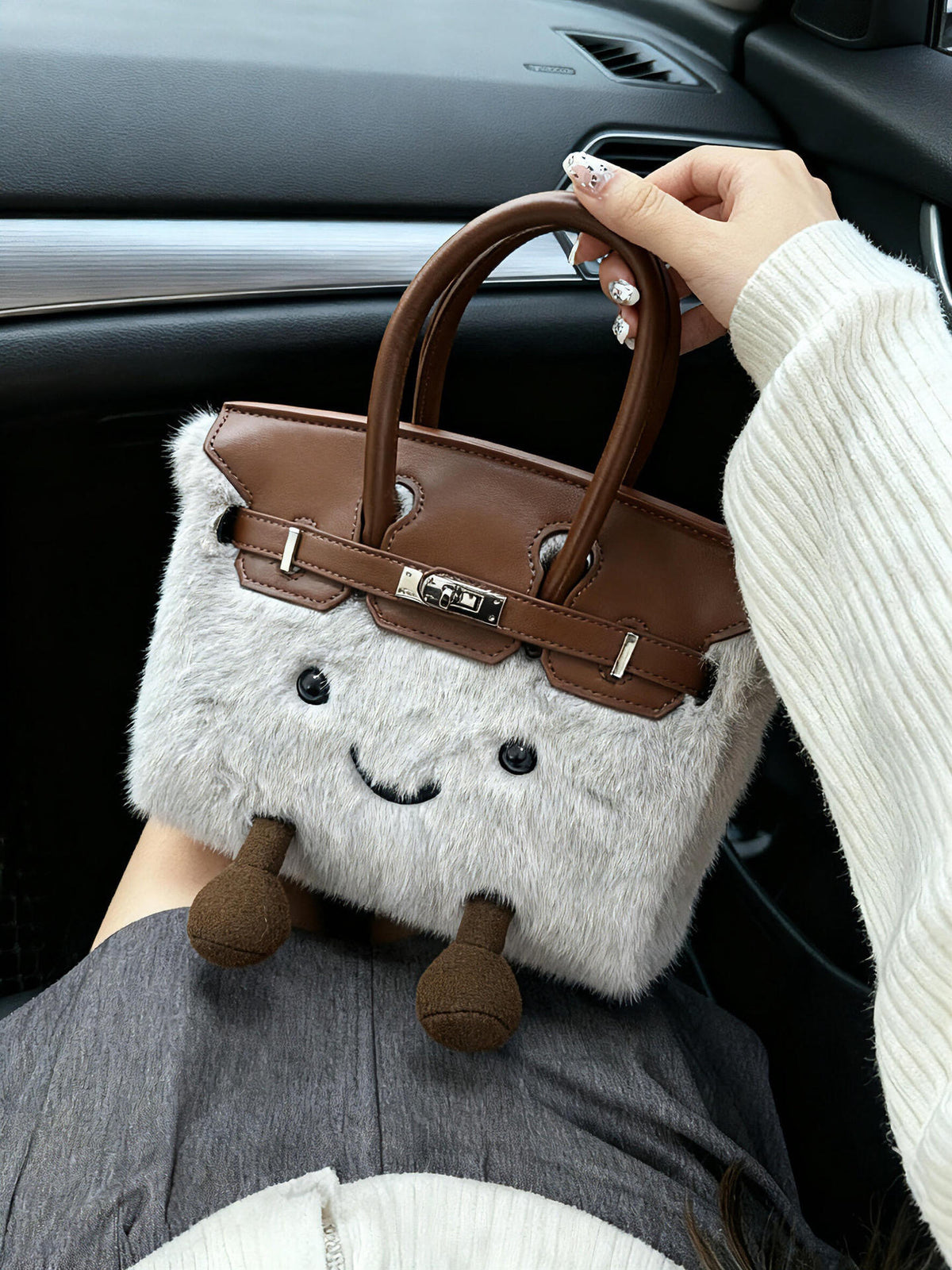Side view of a gray fluffy character handbag with brown trim holding with hand